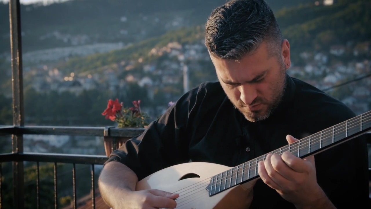 Damir Imamović svira žičani instrument na terasi sa gradom u pozadini